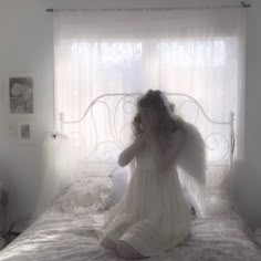 a woman sitting on top of a bed in a room with white walls and curtains