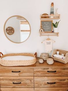 a wooden dresser topped with a baby's crib next to a round mirror