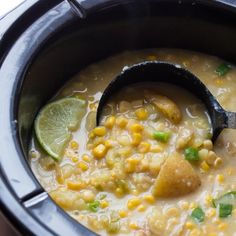 a black spoon in a slow cooker filled with corn and green onions, garnished with cilantro