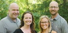 four people posing for a photo in front of trees