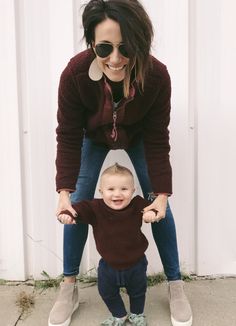 a woman holding the hand of a toddler who is standing on one foot and smiling at the camera