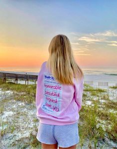 a woman standing on the beach looking out at the ocean with her back to the camera