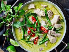 a pan filled with green vegetables and meat on top of a table next to limes