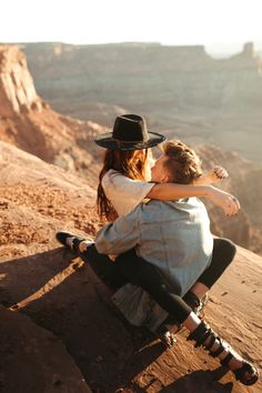 a man and woman sitting on the edge of a cliff with their arms around each other