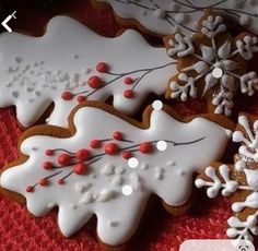 some decorated cookies are sitting on a red tablecloth with snowflakes and berries