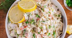 a white bowl filled with chicken salad next to lemon wedges and parsley on the side