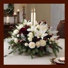 a christmas centerpiece with white and red flowers, greenery and candles on a dining room table