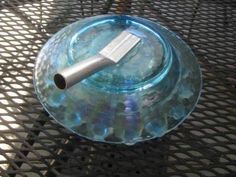 a blue glass plate with a metal object on it's side sitting on a table