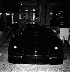 a black sports car is parked in front of a building at night with its lights on