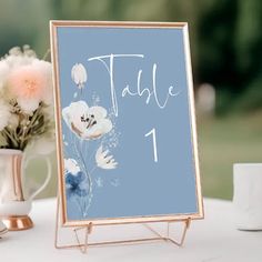 a table sign sitting on top of a white table next to a vase filled with flowers