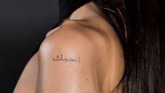 the back of a woman's shoulder with an arabic script tattoo on her left arm