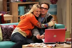 a man and woman sitting on a couch looking at a laptop computer screen while they hug each other