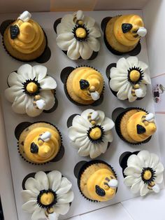 twelve cupcakes with yellow frosting and white flowers in a box on the table