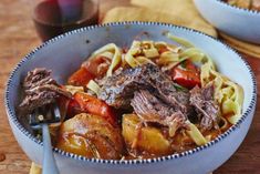 two bowls filled with beef and pasta on top of a wooden table next to a glass of wine