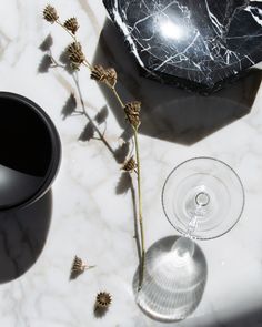 a marble table topped with a wine glass next to a vase filled with dried flowers