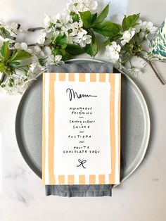 a menu on a plate next to flowers and a vase with white flowers in it