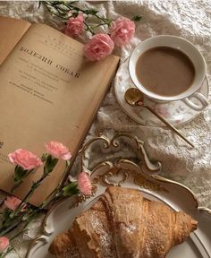 an open book next to a cup of coffee and croissant