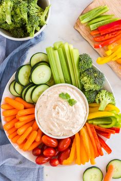 a platter filled with vegetables and dip surrounded by cucumbers, carrots, celery, broccoli