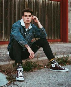 a young man sitting on the curb with his foot up to his face, wearing black and white converse shoes