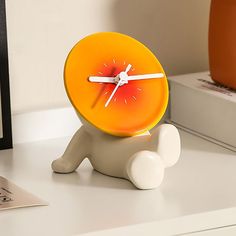 an orange clock sitting on top of a white desk