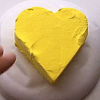 a yellow heart painted on top of a white plate with someone's hand next to it