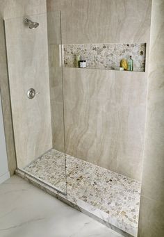 a walk in shower sitting next to a white wall with shelves on the side and glass doors