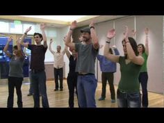 a group of people standing in a room with their hands up to the ceiling and arms raised