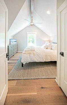 an attic bedroom with white bedding and wooden flooring on the walls, along with two doors leading to another room