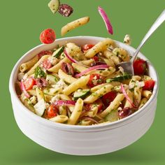 a white bowl filled with pasta and veggies on top of a green background