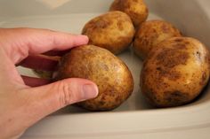 a hand picking up potatoes from a white bowl