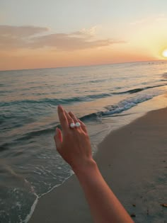 someone is holding their hand up to the sun at the beach as the waves come in