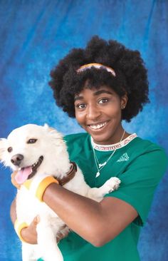 a woman holding a small white dog in her arms and smiling at the camera with an afro hairstyle