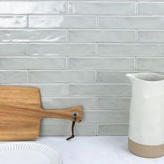 a wooden cutting board sitting on top of a counter next to a white vase and plate