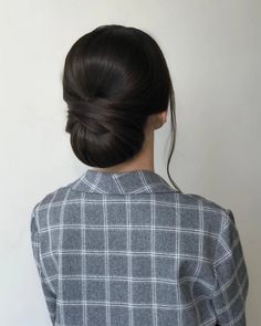 a woman with her hair in a low bun, wearing a grey checkered shirt