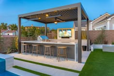 an outdoor bar with stools next to a swimming pool and backyard area at dusk