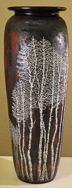 a black and white vase with trees painted on the side, sitting on a table