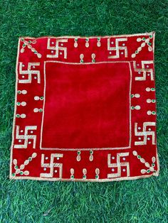 a red rug with white and gold designs on it sitting in the middle of green grass