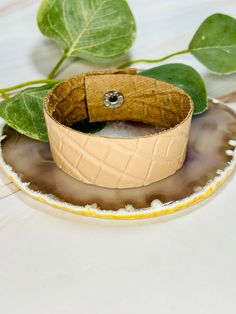 a leather bracelet sitting on top of a plate next to a leafy green plant