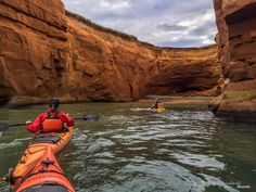 two people in kayaks paddling through the water next to large rocks and cliffs