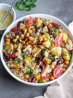 a white bowl filled with vegetables and rice next to a small bowl of sauce on the side