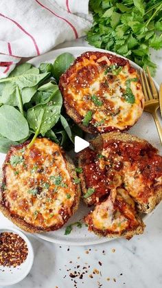 three mini pizzas on a plate with spinach leaves and seasoning next to them