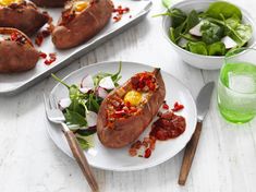 two plates with baked potatoes on them and salad in bowls next to eachother