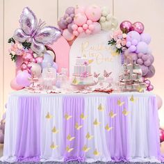 a table topped with lots of pink and purple balloons next to a cake on top of a table