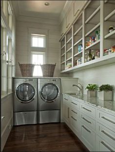 a washer and dryer in a small room with white cabinetry, wood flooring and open shelving