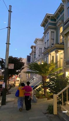 two people walking down the sidewalk in front of some houses