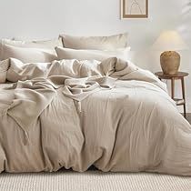 an unmade bed in a white room with beige linens and pillows on it