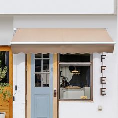 a blue door and window in front of a white building with potted plants next to it