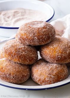 a white plate topped with sugar covered doughnuts next to a bowl of powdered sugar