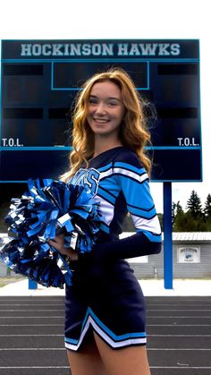 a cheerleader standing in front of a large scoreboard holding a pom pom