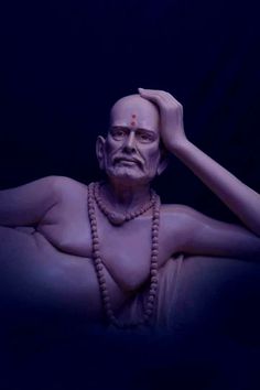 a statue of a man with beads around his neck and hands on his head, in front of a dark background